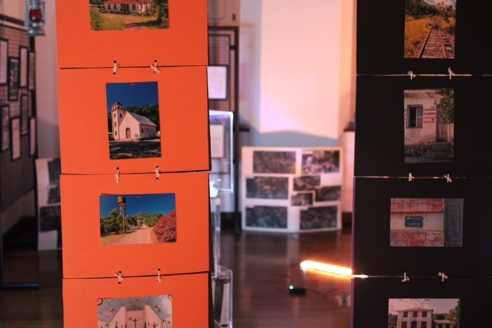 Fotografia de pessoas circulando em espaço de exposição. Em destaque, projeção de vídeo com entrevista na parede.