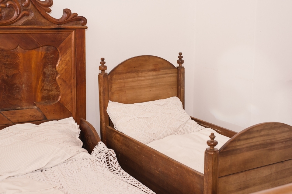 berço de madeira com roupas de cama branca ao lado de uma cama de casal de madeira com roupas de cama brancas