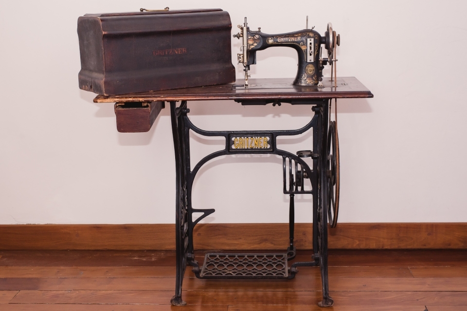frente da máquina de costura atrelada à mesa e sobre a mesa, uma caixa para transporte da máquina de costura